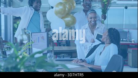 Presenting team celebrating seated coworker in casual business attire at office with balloons Stock Photo