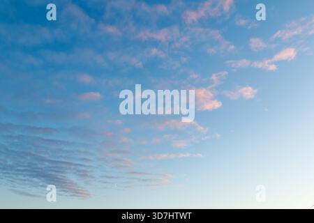 The sky is filled with delicate pastel clouds at dawn or sunset. Pink and purple hues contrast softly against the blue sky. A small crescent moon is v Stock Photo