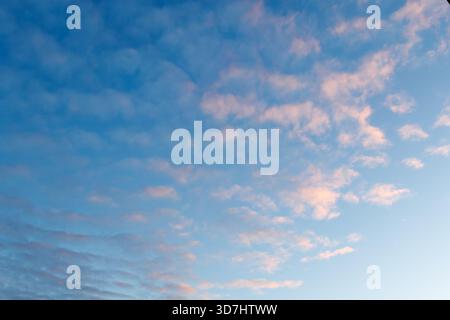 The sky is filled with delicate pastel clouds at dawn or sunset. Pink and purple hues contrast softly against the blue sky. A small crescent moon is v Stock Photo