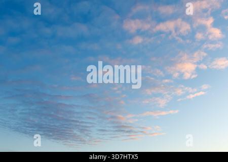 The sky is filled with delicate pastel clouds at dawn or sunset. Pink and purple hues contrast softly against the blue sky. A small crescent moon is v Stock Photo