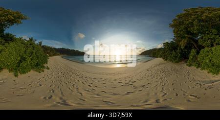 A serene beach with soft sand and footprints, as the sun sets over calm waters, framed by lush greenery. Petite Anse, Seychelles. VR 360. Stock Photo