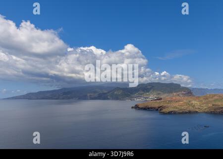 View from Ponta Sao Lourenco Madeira to mainland with wind turbines and panels, showing calm water and soft clouds across distant green mountains Stock Photo