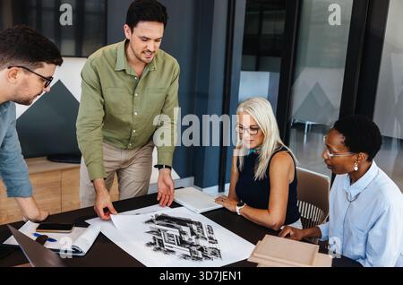 A group of professionals collaborates on a project in a contemporary workplace, reviewing plans. Stock Photo