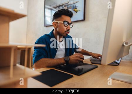A focused male professional uses a digital drawing tablet while working on architectural projects in a modern office. Creativity, concentration, and t Stock Photo