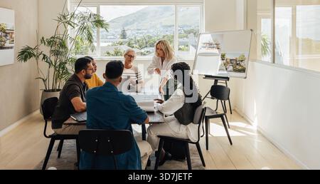 Architects collaborating on a project around a table in a scenic office space. The diverse group consists of professionals discussing concepts with de Stock Photo