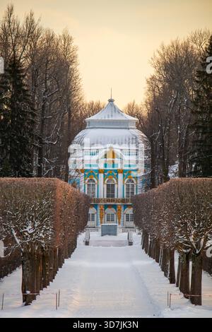 Saint Petersburg - December 13, 2024: The blue and white Hermitage Pavilion in Catherine Park, seen down a snowy path lined by trimmed trees and dense Stock Photo