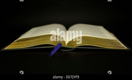 Open book with blue bookmark on black background Stock Photo