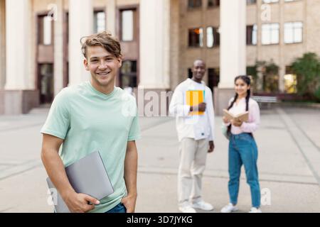 Group of Students Enjoying a Sunny Day on Campus With Laptops and Books in Hand Engaging in Study Activities Together Stock Photo