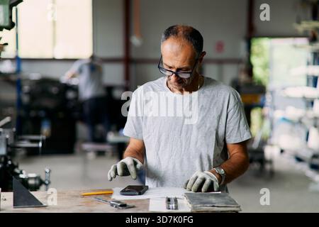 Craftsman Inspecting Smartphone On Workbench In Workshop With Tools Pe Stock Photo