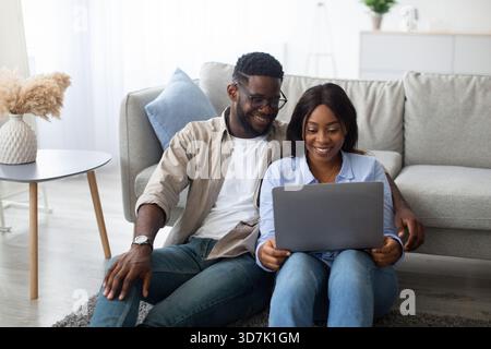 Happy Couple Enjoys Time Together Using Laptop While Relaxing in Living Room Stock Photo