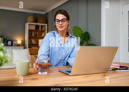 Healthcare professional conducts telemedicine session on laptop reviewing patient paperwork and typing notes while a stethoscope lies on the desk conv Stock Photo