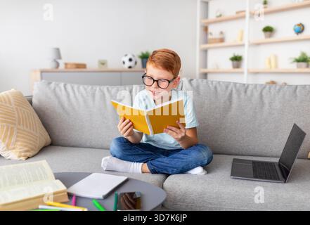 Preteen Boy Studies at Home Using Laptop and Books During Lockdown With Cheerful Focus Stock Photo