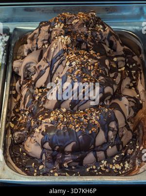 Rich chocolate gelato topped with chocolate sauce and chopped hazelnuts in a metal display container. A sweet dessert Stock Photo