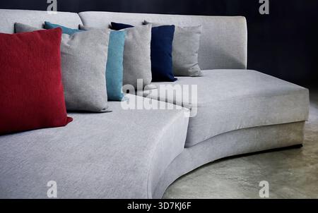 Interior design furniture concept. Close-up of a contemporary light grey sectional couch featuring a vibrant red scatter cushion alongside teal and bl Stock Photo
