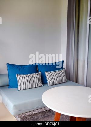 Home decoration and relaxation concept. Vertical view of a semi-outdoor terrace corner featuring a built-in stone texture couch with blue and striped Stock Photo