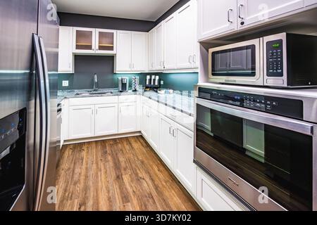 Modern kitchen with white cabinets, marble countertops, and stainless steel appliances. Stock Photo