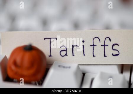 tariff written on paper, resting on a white keyboard with a blurred decorative miniature pumpkin. Depicts global trade, economics, and Halloween, seas Stock Photo