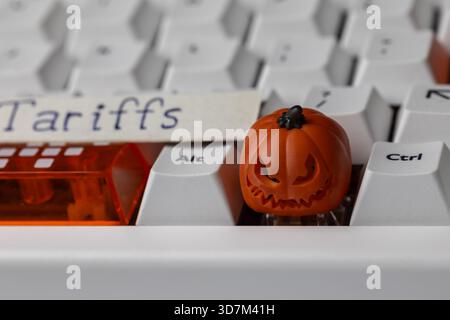scary jack-o'-lantern keycap sits on a clean mechanical keyboard, next to an orange shift key and a paper tag with the word 'tariffs,' symbolizing tra Stock Photo