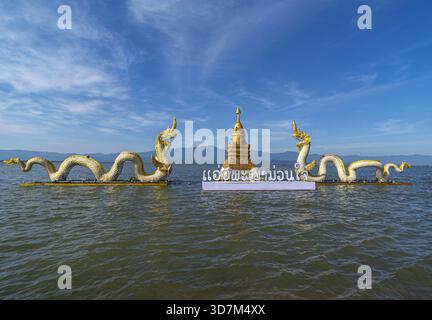 Muang, Phayao, Thailand – November 25, 2025: Kwan Phayao Lake - Two golden great Naga statues flank a golden stupa on floating platforms in a lake und Stock Photo