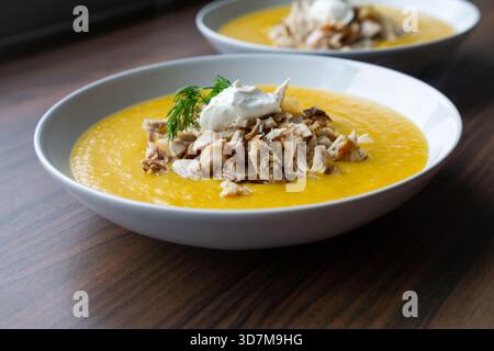 This macro image focuses on the intricate textures of pumpkin soup and chicken topping. Stock Photo
