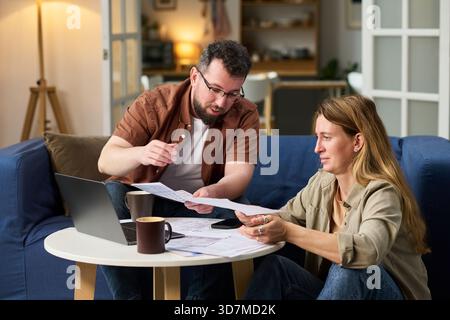 Caucasian middle aged man and Caucasian middle aged woman sitting at table reviewing financial documents and using laptop Stock Photo