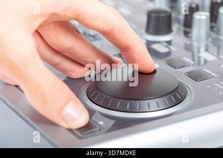 Hand using a generic jog wheel on audio video mixer console or DJ equipment finger adjusting shuttle dial for mixing and playback control professional Stock Photo
