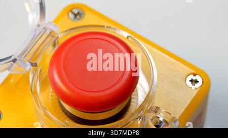 Red emergency stop push button with clear protective cover open enclosure, industrial mushroom switch on machinery control panel, safety shutdown devi Stock Photo