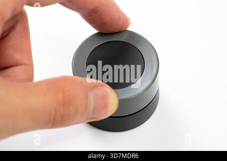 Man adjusting a simple generic round gray knob with his fingers, object isolated on white background, rotary control dial for electronics settings, cl Stock Photo