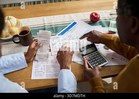 Middle aged Black man and middle aged Black woman reviewing tax documents together at table, using calculator and receipts, discussing financial paperwork related to paying taxes Stock Photo