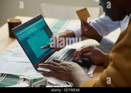 Middle aged Black man using laptop for online tax payment while middle aged Black woman holding credit card and pointing at computer screen, tax documents and cash on table Stock Photo