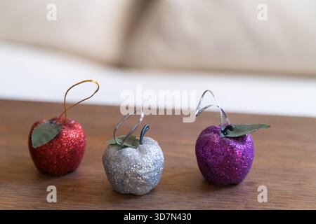 three sparkling apple christmas ornaments on wood with blurred sofa in background Stock Photo
