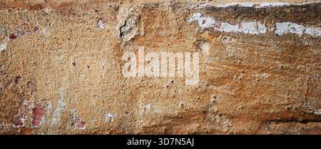 Old cracked brick wall with  peeling plaster and rough textured surface, showing natural aging and rustic imperfections. Stock Photo