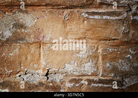 Old cracked brick wall with  peeling plaster and rough textured surface, showing natural aging and rustic imperfections. Stock Photo