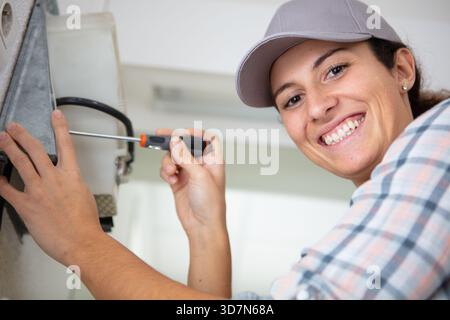 happy female builder with screwdriver fixing dispenser to wall Stock Photo