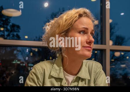 A young woman with curly hair, dressed in a light green jacket, enjoys a serene moment in a cafe, looking Stock Photo