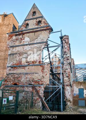Crumbling brick building facade supported by metal reinforcement frames, showing urban preservation efforts on an old historic structure Stock Photo