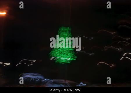 An abstract motion blur of a green glowing Christmas tree at night, creating a festive light leak overlay effect. Stock Photo