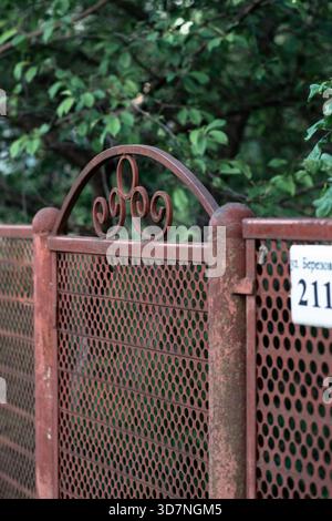 Rusty metal gate with decorative ironwork and house number plate in a residential area, Russia. Stock Photo