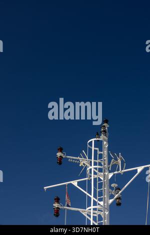 A close view of a white ship mast with navigation lights and rigging set against a bright blue sky, conveying nautical technology, safety, and maritim Stock Photo