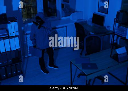 Thief with gun and briefcase in office at night Stock Photo