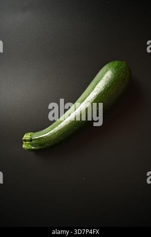 Top-down shot of a single, fresh, glossy green zucchini placed diagonally on a minimalist black background. Ideal for themes of healthy eating, vegani Stock Photo