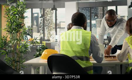 Site developers and architects in business meeting reviewing blueprints and structural designs. Team discusses redevelopment and city planning for residential project growth. Stock Photo