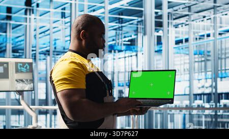 Engineer using green screen laptop in industry 4.0 industrial plant to install machinery. Robotics technician using mockup notebook in smart factory calibrating IoT sensors, panning shot Stock Photo