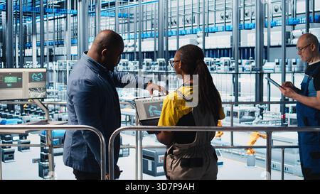 Engineers meeting with smart factory investor, showing insights based on collected data. Specialists discussing with industrial plant shareholder, presenting metrics gathered by sensors, camera A Stock Photo