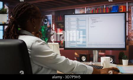 System administrator types code into PC, developing software, entering commands. IT professional at home fixing errors in application, implementing new features, listening music, camera A jib up shot Stock Photo