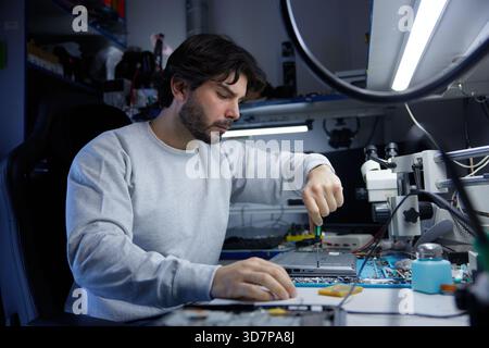 A technician is carefully repairing a circuit board with precision tools in a workshop Stock Photo