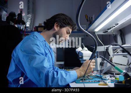 A skilled technician diligently repairing laptop while working under a microscope Stock Photo