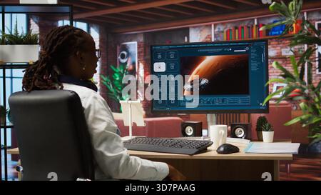 Woman using AI program turning text prompt into videos, pleased by results. Person surrounded by plants interacting with text to video artificial intelligence generative model, camera A Stock Photo