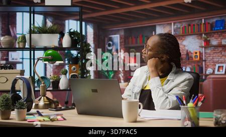 Fatigued woman daydreaming, gazing outside the window, feeling bored after working too much on job tasks. Contemplative person at home caught in thoughts, pondering, camera A Stock Photo