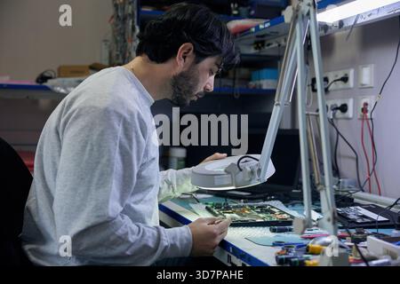 A man is working on a motherboard with a magnifying glass Stock Photo